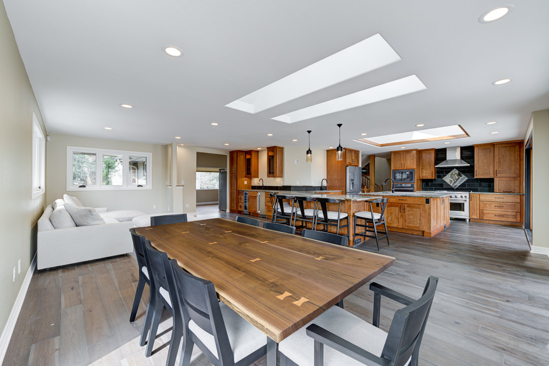 Open kitchen with custom cabinetry, live-edge dining table, and skylights